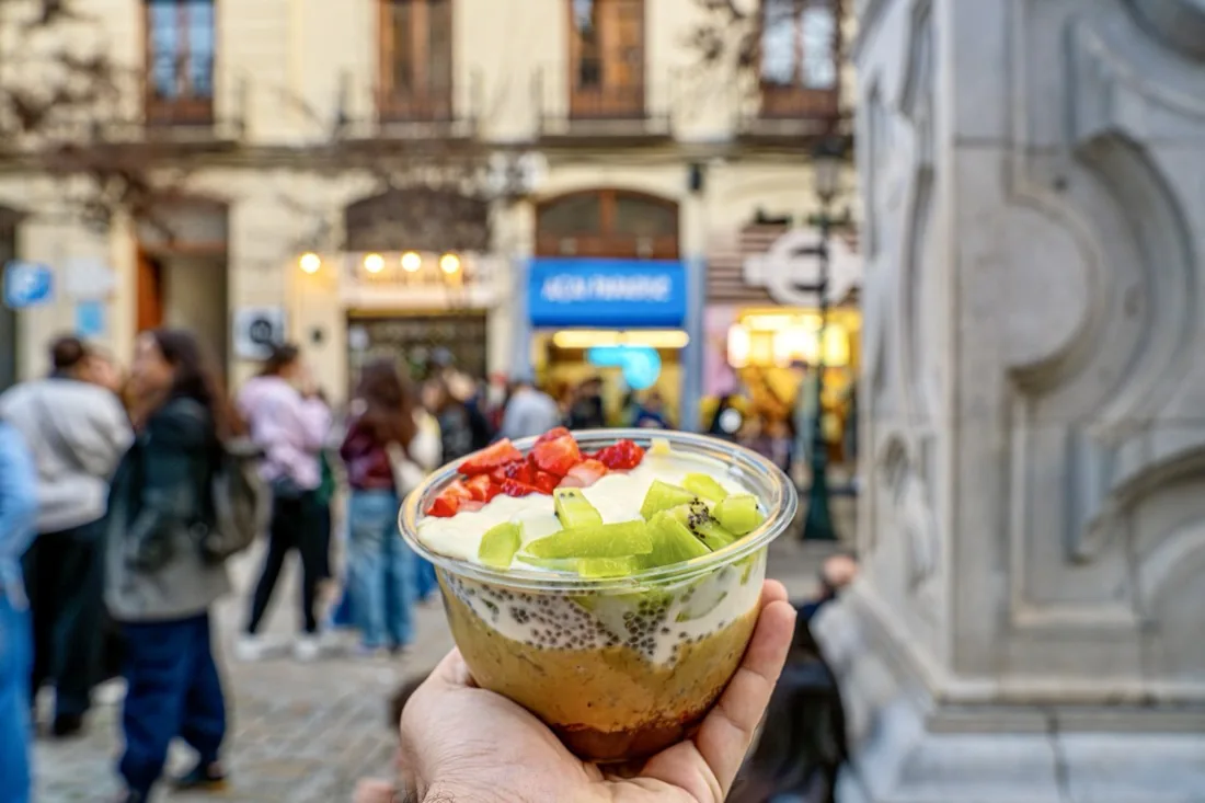 Bowl de açaí en la mano con la tienda de Açaí Paradise Granada al fondo