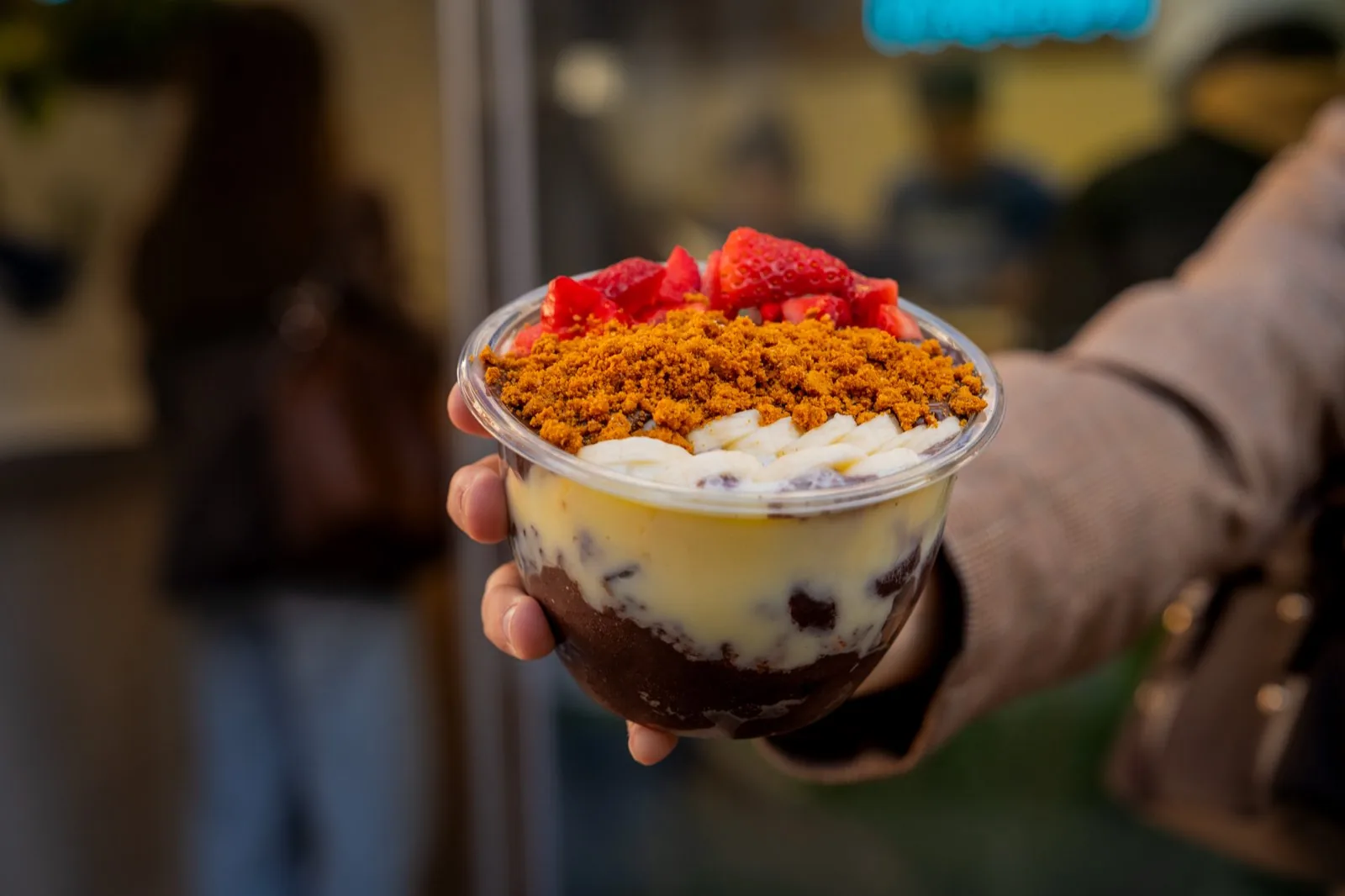 Acai bowl con capas de açaí, crema, fresa y granola en la mano