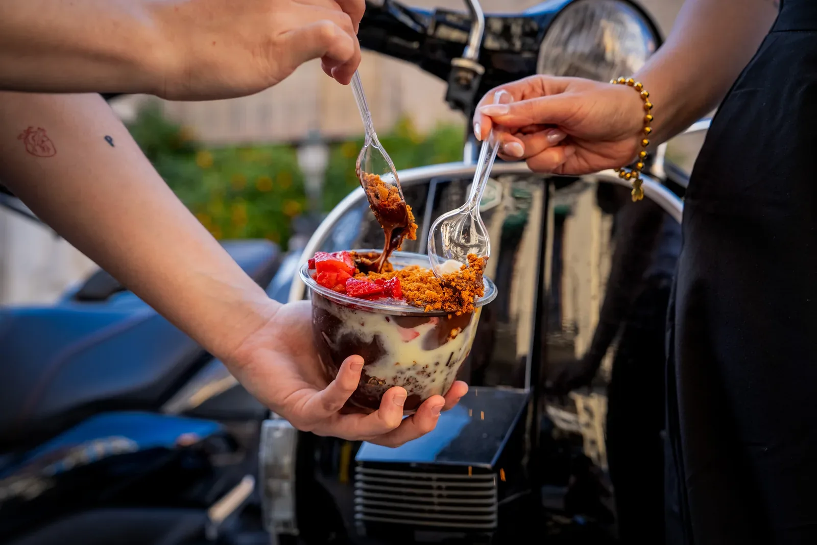Dos personas compartiendo un bowl de açaí apoyadas en una moto